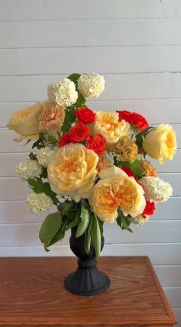 Yellow garden roses, red roses and white blooms arranged in a black urn