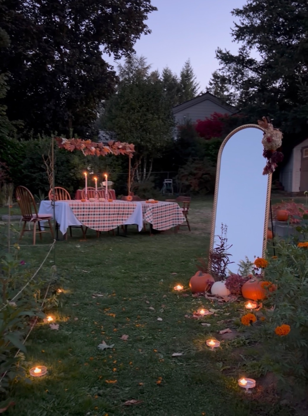 The garden at dusk with tealights in the grass, pumpkins, a mirror and candlelit tables